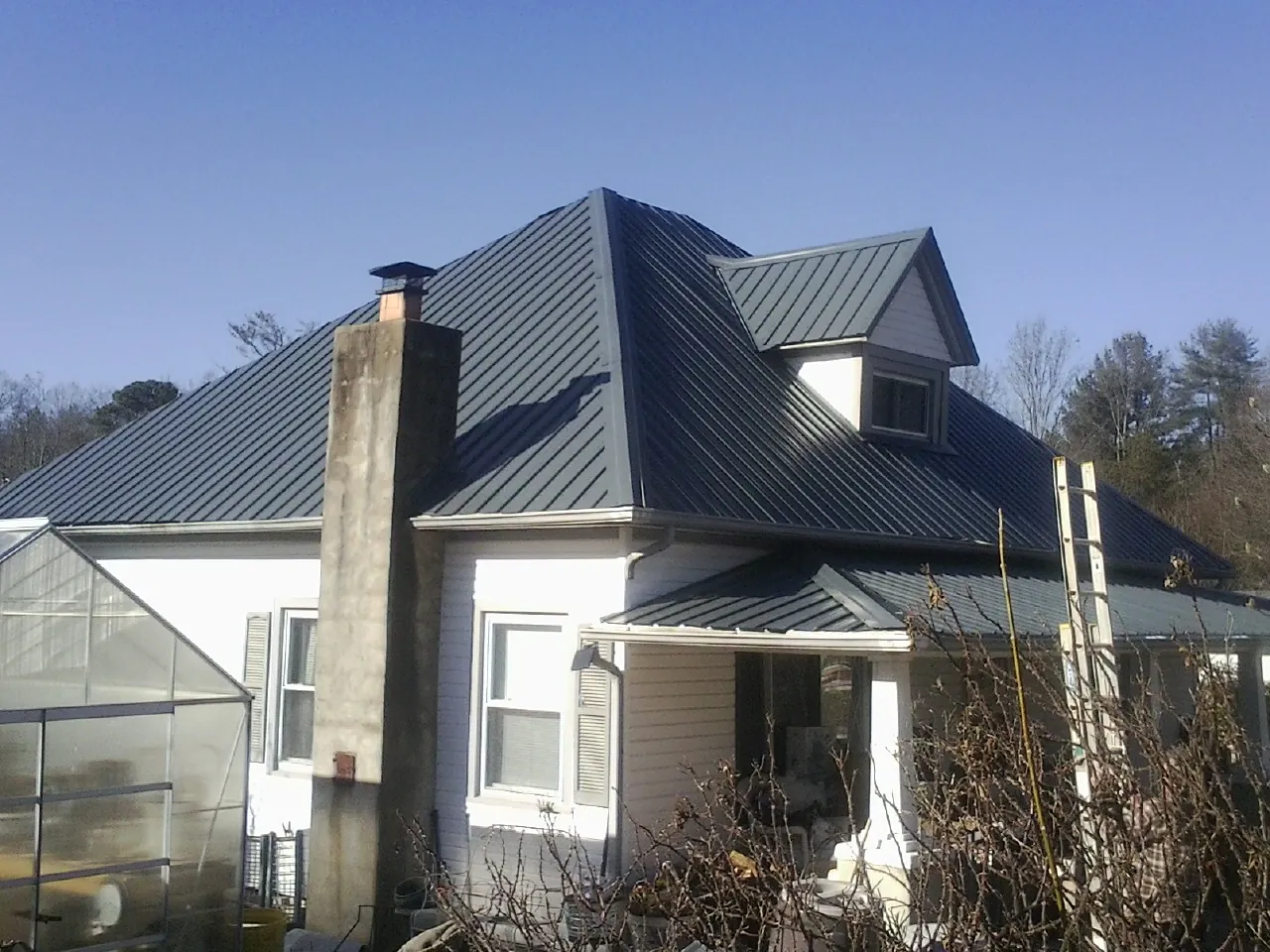 Dark blue standing seam metal roof on a white farmhouse with dormer — Slate & Tile Roof Repair by Roofing Brothers in Nye
