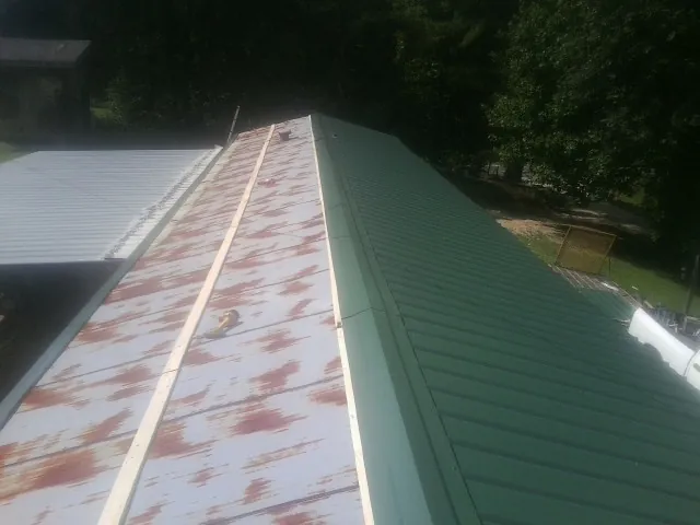 Old rusted panels beside newly installed green metal roofing — Wind Damage Roof Repair by Roofing Brothers in Nye