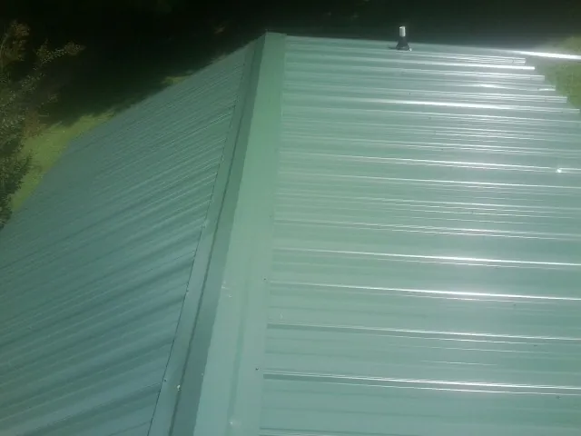 New green metal panels meeting at the ridge of a roof — Flat Roof Repair work by our crew in Nye