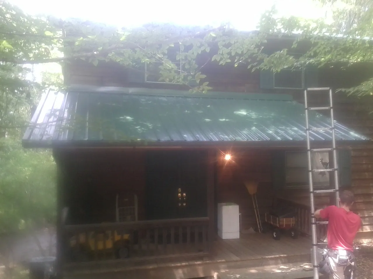 Worker on a ladder at the green porch roof of a wooded cabin in Nye