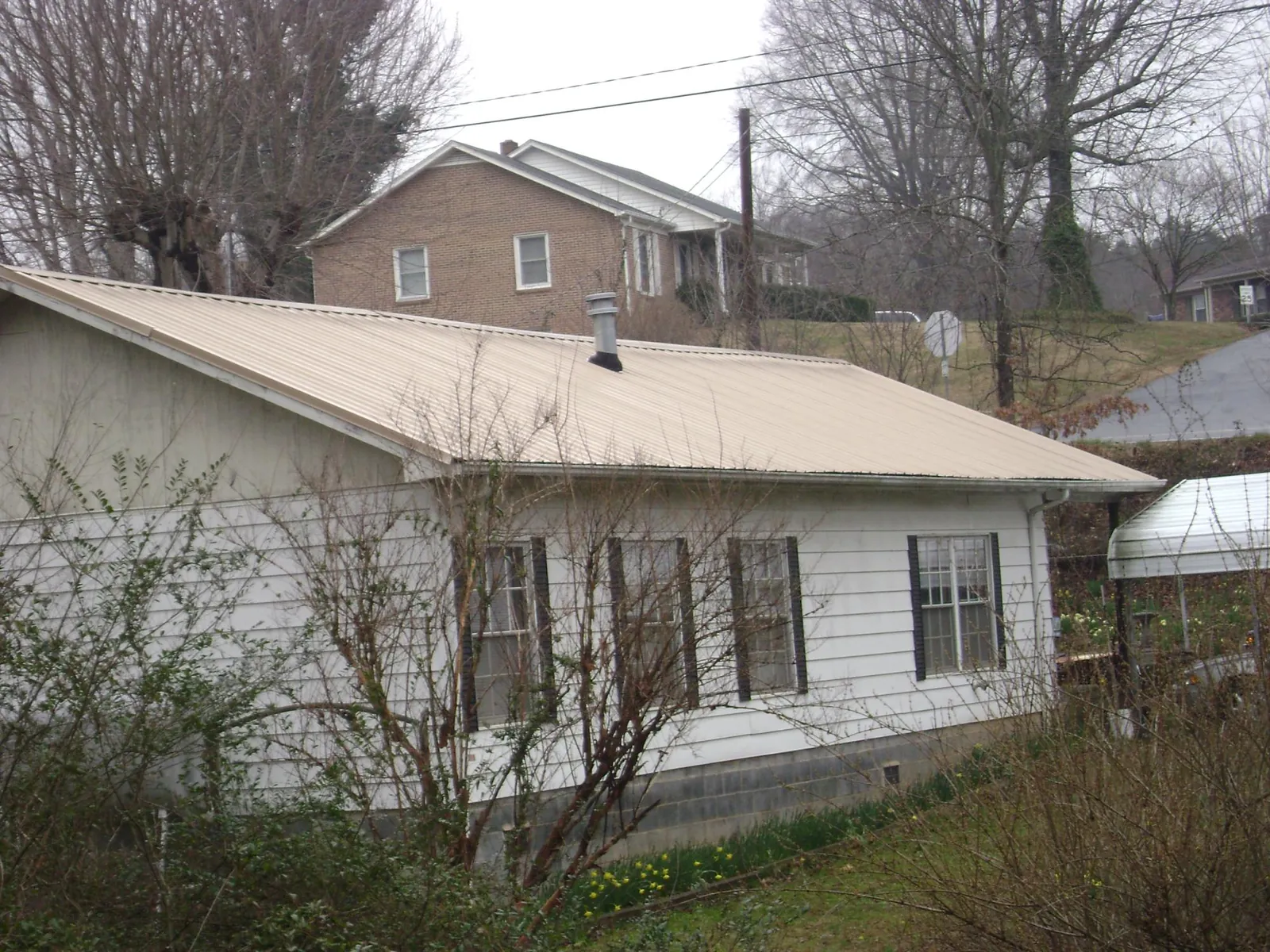 Tan metal roof on a white sided house set into a hillside — Commercial Roofing by Roofing Brothers in Nye
