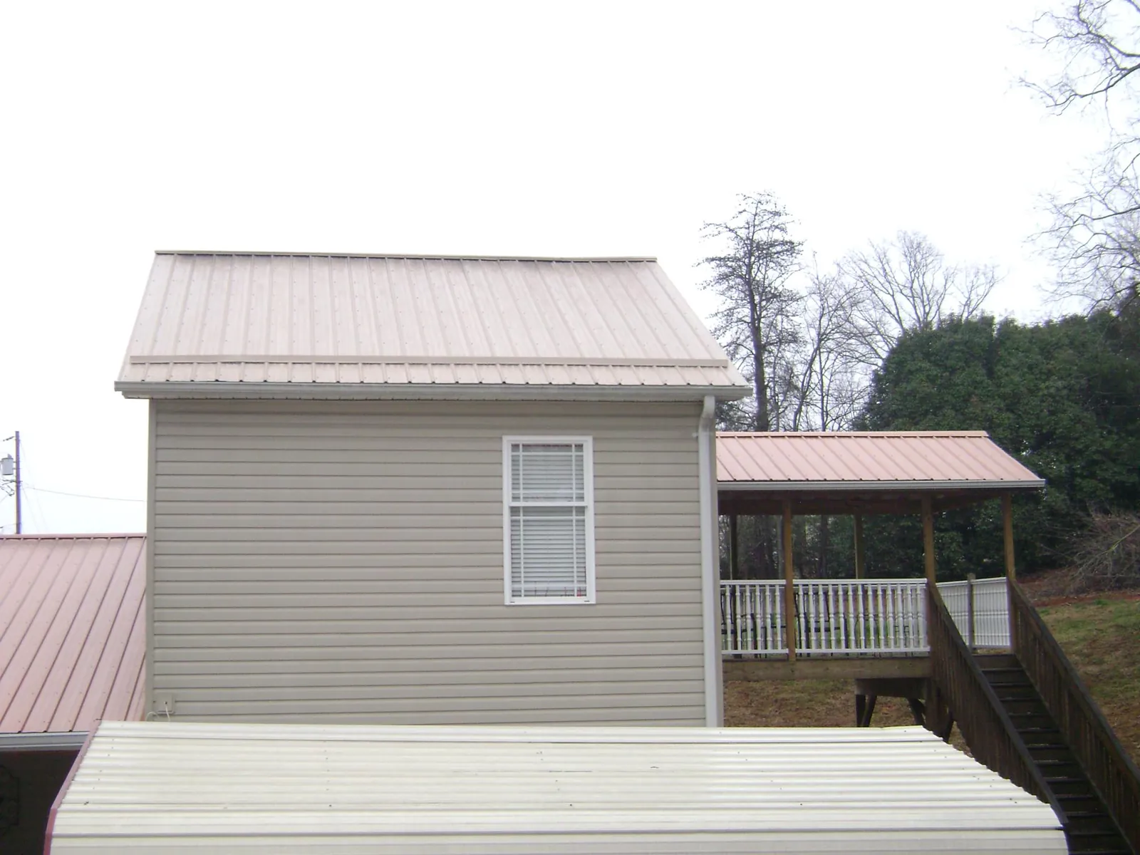 Tan metal roofs on a two story addition and attached porch, from a Roof Replacement job in Nye
